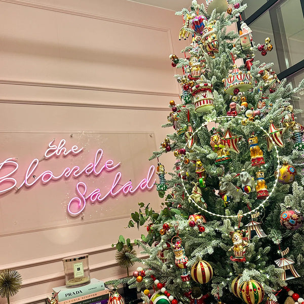 Albero di Natale innevato con decorazioni colorate in uno spazio commerciale con insegna al neon
