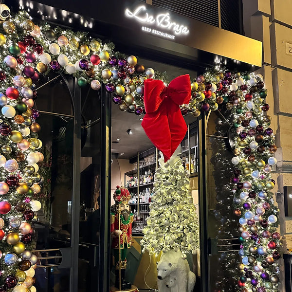 Arco di palline natalizie con fiocco rosso all'ingresso di un ristorante