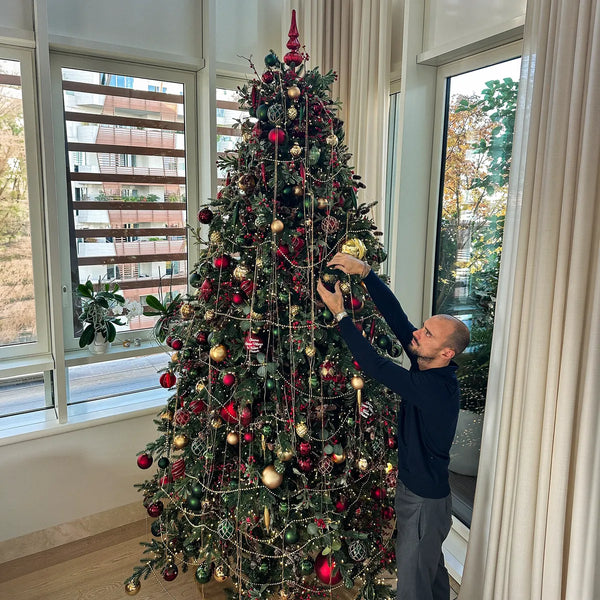 Albero di Natale rosso e oro accanto a grandi vetrate durante l'allestimento